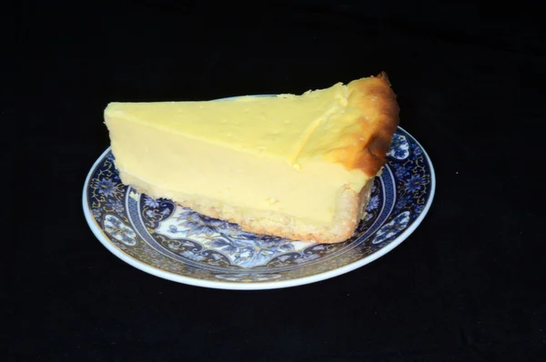 Un pedazo de pastel de queso sobre un hermoso platillo sobre un fondo negro — Foto de Stock