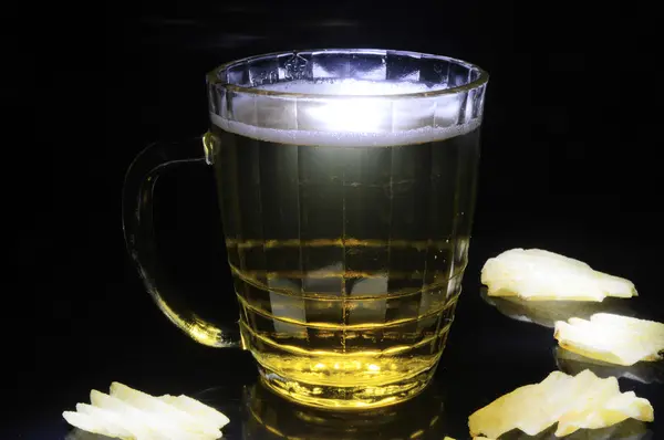 Mug of beer and chips on a black background — Stock Photo, Image