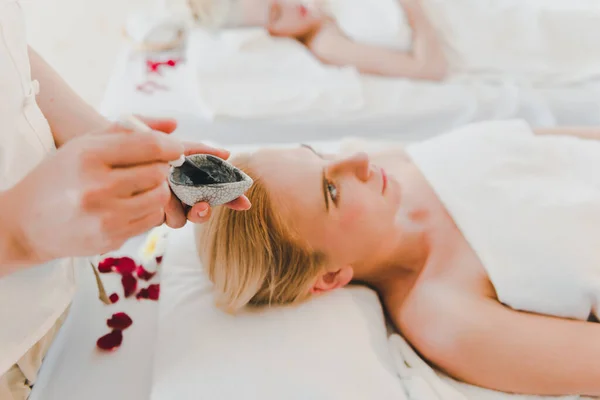 A young woman using a black mud mask in the spa. For facial treatment by spa staff.