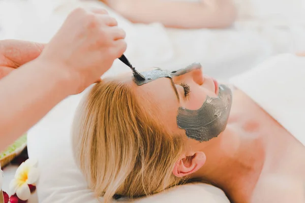 A young woman using a black mud mask in the spa. For facial treatment by spa staff.