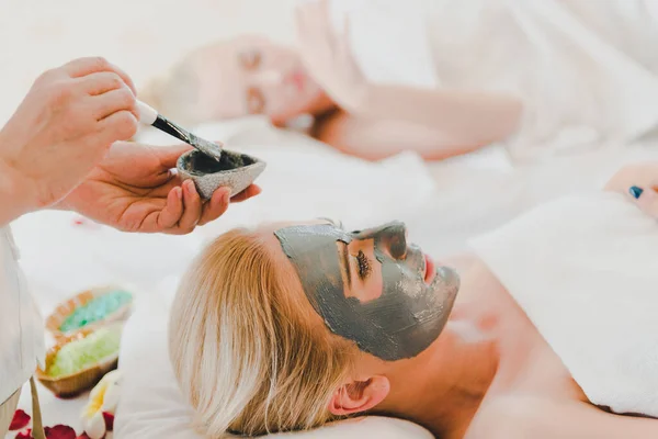 A young woman using a black mud mask in the spa. For facial treatment by spa staff.