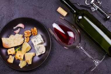 Cam ve şişe kırmızı şarap, peynir, ekmek, sarımsak, fındık, salam gri taş doku arka plan üzerinde