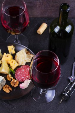 Cam ve şişe kırmızı şarap, peynir, ekmek, sarımsak, fındık, salam gri taş doku arka plan üzerinde