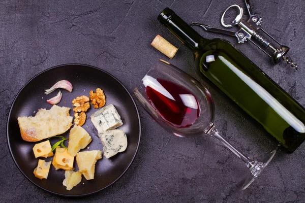 Glass and bottle of red wine, cheese, bread, garlic, nuts, salami on gray stone texture background — Stock Photo, Image