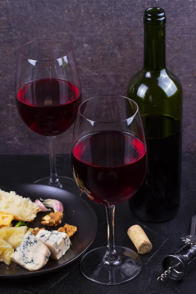 Glass and bottle of red wine, cheese, bread, garlic, nuts, salami on gray stone texture background — Stock Photo, Image