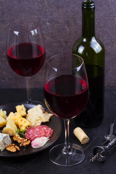 Cam ve şişe kırmızı şarap, peynir, ekmek, sarımsak, fındık, salam gri taş doku arka plan üzerinde