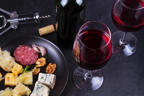 Glass and bottle of red wine, cheese, bread, garlic, nuts, salami on gray stone texture background — Stock Photo, Image