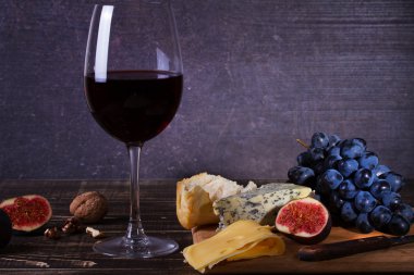 Meyve, peynir, incir ve koyu ahşap zemin üzerine fındık ile kırmızı şarap cam