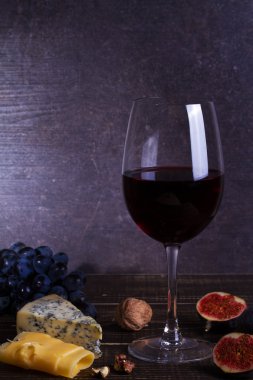Meyve, peynir, incir ve koyu ahşap zemin üzerine fındık ile kırmızı şarap cam