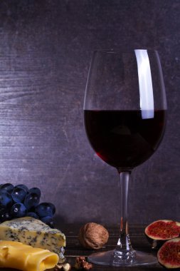 Meyve, peynir, incir ve koyu ahşap zemin üzerine fındık ile kırmızı şarap cam