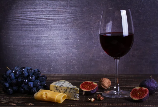 Red wine glass with fruits, cheese, figs and nuts on dark wooden background — Stock Photo, Image