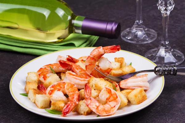 Shrimp with crispy croutons and scallions in white plate. White wine bottle — Stock Photo, Image