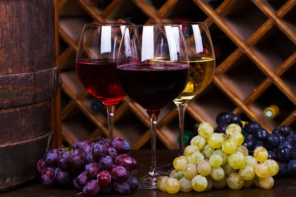 Bicchieri rossi, rosati e bianchi e bottiglie di vino con uva in cantina — Foto Stock