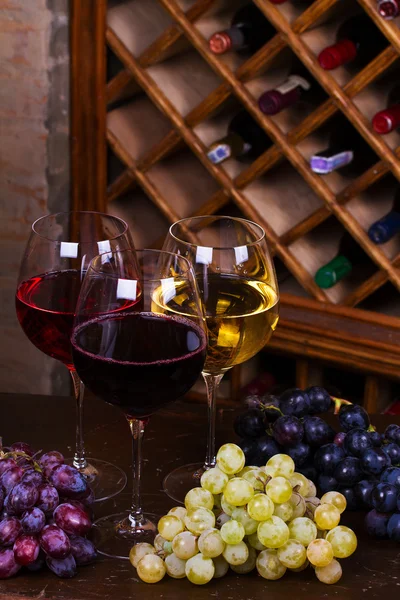 Rote, rosa und weiße Gläser und Flaschen Wein mit Trauben im Weinkeller — Stockfoto
