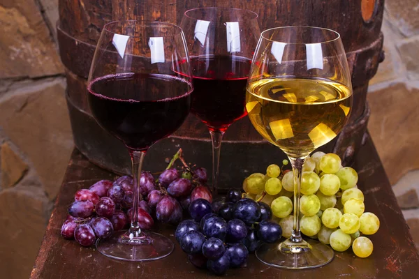 Bicchieri rossi, rosati e bianchi e bottiglie di vino con uva in cantina — Foto Stock