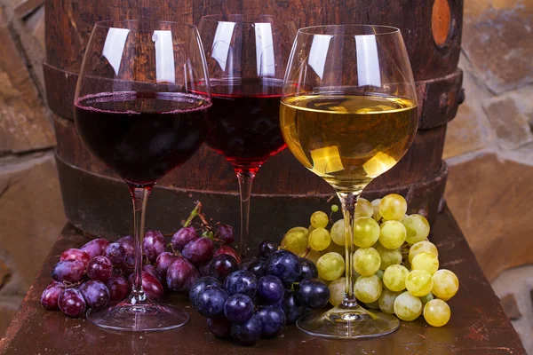 Red, rose and white glasses and bottles of wine with grapes in wine cellar — Stock Photo, Image