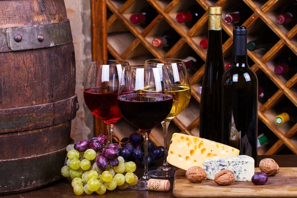 Red, rose and white glasses and bottles of wine with grapes in wine cellar — Stock Photo, Image