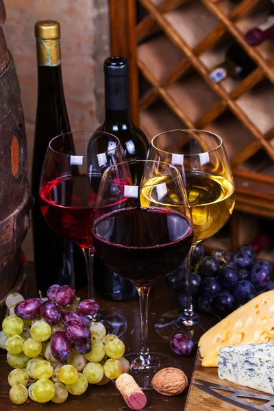 Bicchieri rossi, rosati e bianchi e bottiglie di vino con uva in cantina — Foto Stock