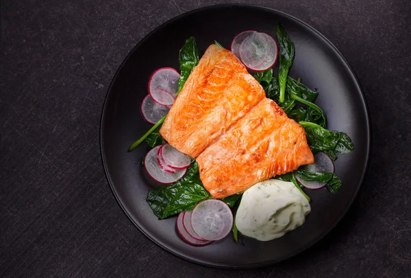 Broiled salmon with radish and spinach, served on black plate — Stock Photo, Image