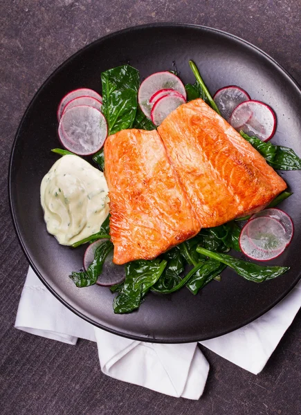 Broiled salmon with radish and spinach, served on black plate — Stock Photo, Image