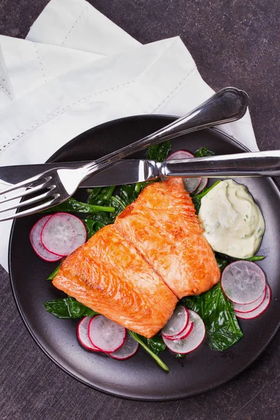 Broiled salmon with radish and spinach, served on black plate — Stock Photo, Image