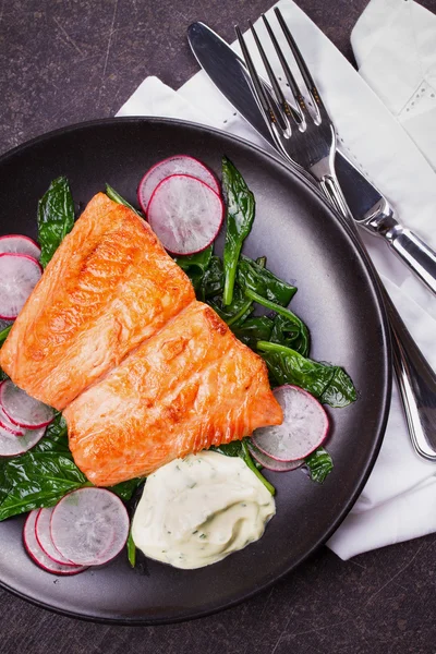 Broiled salmon with radish and spinach, served on black plate — Stock Photo, Image