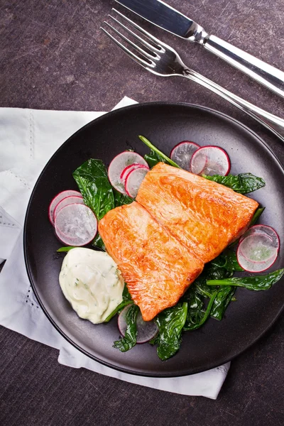 Broiled salmon with radish and spinach, served on black plate — Stock Photo, Image