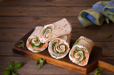 Somon ve krem peynirli dürüm. Tütsülenmiş somon, fesleğen ve roket salatalı rulo. Servis panosunda burrito