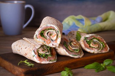 Somon ve krem peynirli dürüm. Tütsülenmiş somon, fesleğen ve roket salatalı rulo. Servis panosunda burrito