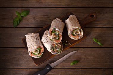 Somon ve krem peynirli dürüm. Tütsülenmiş somon, fesleğen ve roket salatalı rulo. Servis kurulunda burrito. Yukarıdan görüntüle, en üstten