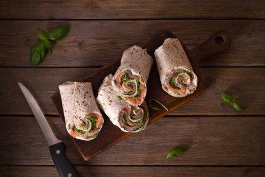 Somon ve krem peynirli dürüm. Tütsülenmiş somon, fesleğen ve roket salatalı rulo. Servis panosunda burrito