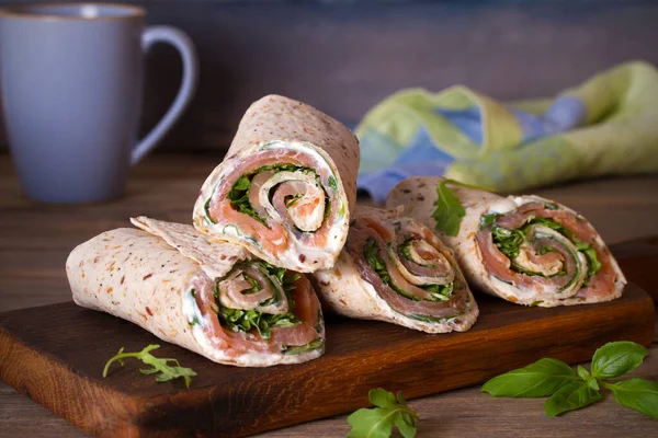 Somon ve krem peynirli dürüm. Tütsülenmiş somon, fesleğen ve roket salatalı rulo. Servis panosunda burrito