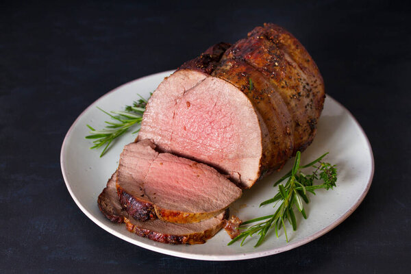 Roasted beef with herbs on dark background