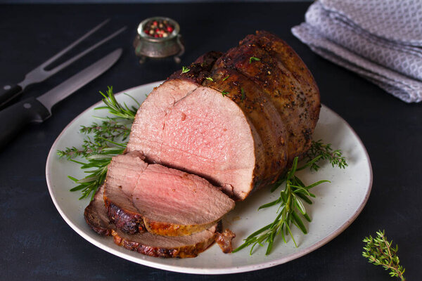 Roasted beef with herbs on dark background