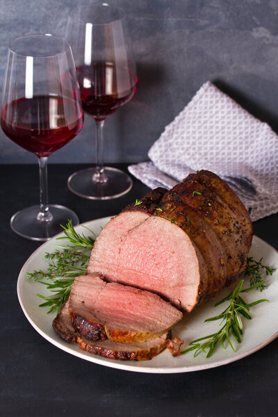 Roasted beef with herbs and red wine on dark background