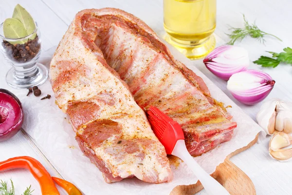 Fresh pork ribs, meat prepared for roast with garlic, parsley, onion and red chili pepper on wooden background — Stock Photo, Image