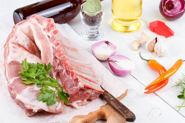 Costolette di maiale fresche, carne preparata per arrosto con aglio, prezzemolo, cipolla e peperoncino rosso su fondo di legno — Foto Stock