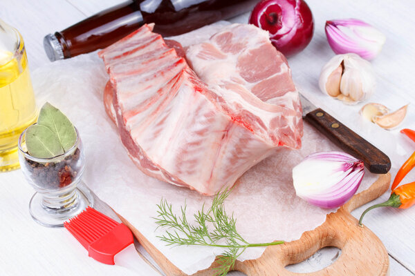 Fresh pork ribs, meat prepared for roast with garlic, parsley, onion and red chili pepper on wooden background