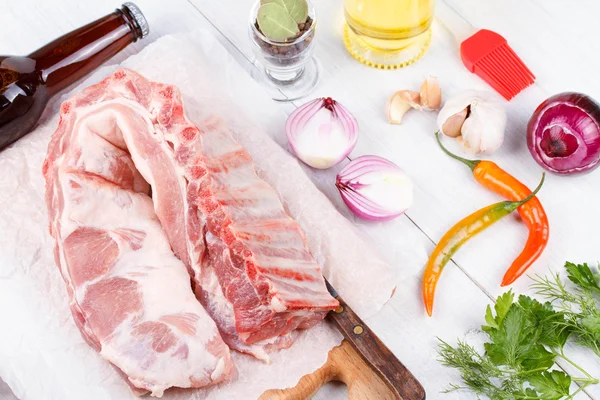 Frische Schweinerippchen, Fleisch zum Braten mit Knoblauch, Petersilie, Zwiebeln und roter Chilischote auf Holzboden — Stockfoto