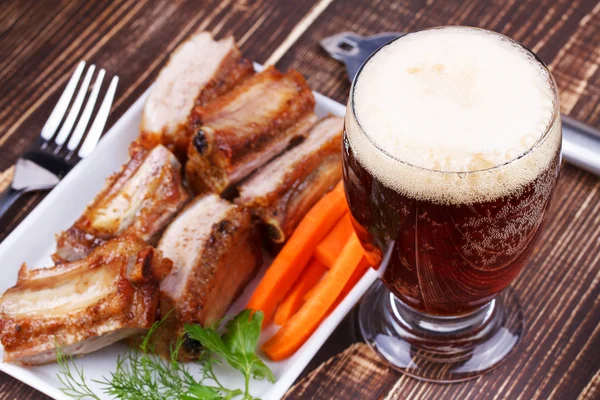 Glas bier. Gegrilde varkensribbetjes en verse wortel op houten achtergrond — Stockfoto
