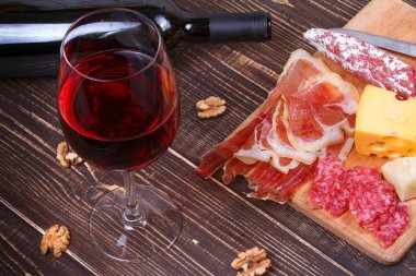 Glass and bottle of wine, cheese and prosciutto on wooden background. Still life clipart