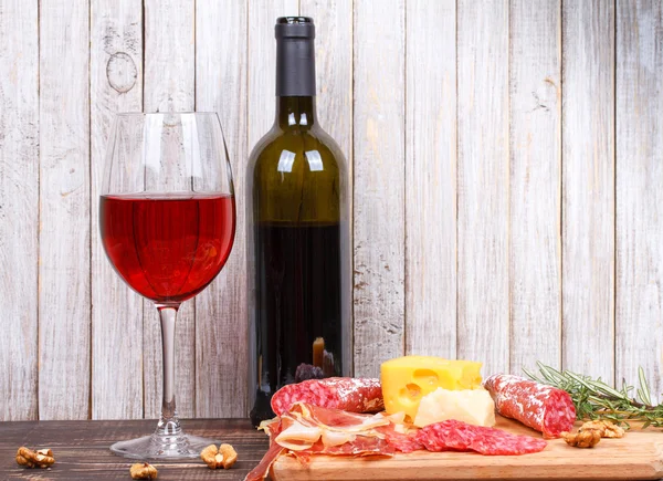 Glass and bottle of wine, cheese and prosciutto on wooden background. Still life — Stock Photo, Image