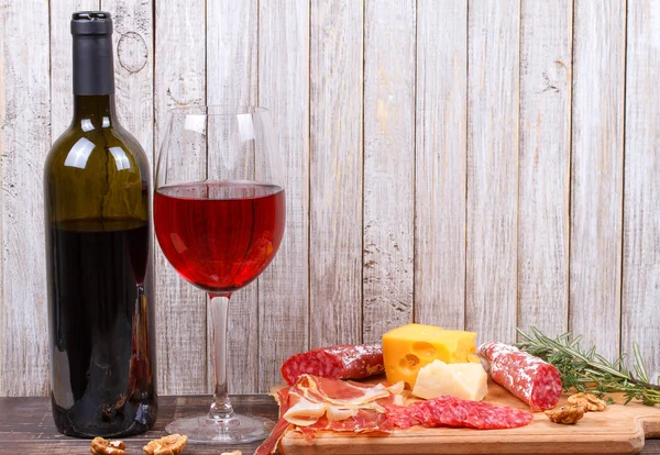 Glass and bottle of wine, cheese and prosciutto on wooden background. Still life