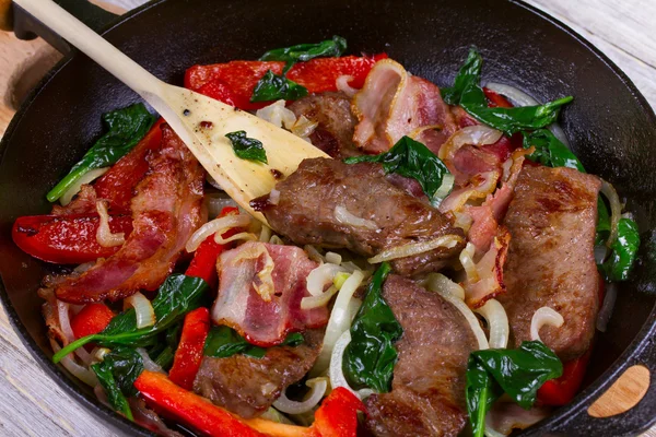 Frigideira com carne frita, bacon, pimentão vermelho e espinafre — Fotografia de Stock