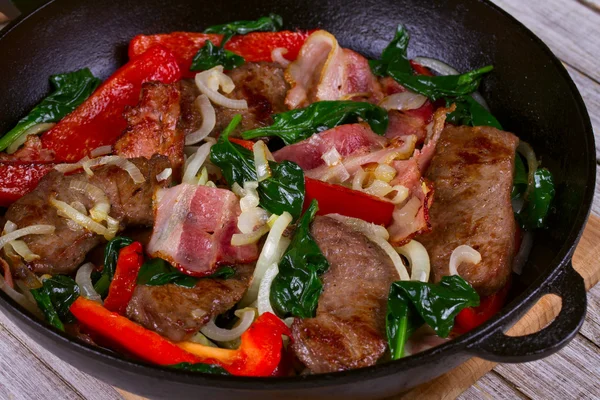 Frigideira com carne frita, bacon, pimentão vermelho e espinafre — Fotografia de Stock