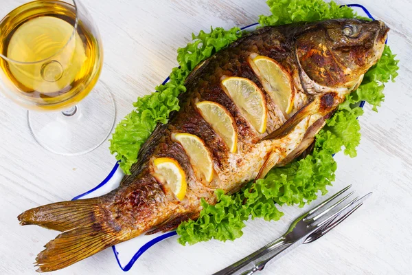 Carpa entera de pescado a la parrilla servida con ensalada y limón; copa de vino —  Fotos de Stock