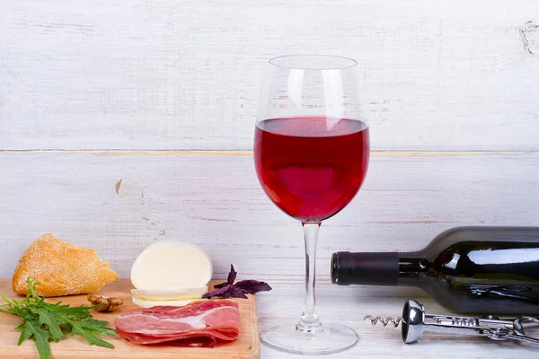 Glass and bottle of wine, cheese and prosciutto. — Stock Photo, Image