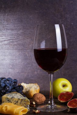 Bardak kırmızı şarap, peynir, üzüm, ceviz, incir, Erik ve elma ahşap arka plan üzerinde