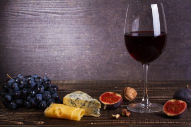 Bardak kırmızı şarap, peynir, üzüm, ceviz, incir, Erik ve elma ahşap arka plan üzerinde