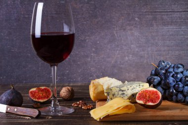 Bardak kırmızı şarap, peynir, üzüm, ceviz, incir, Erik ve elma ahşap arka plan üzerinde